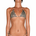 A woman modeling a zebra-print string bikini with a triangle top and matching side-tie bottoms against a plain white background.