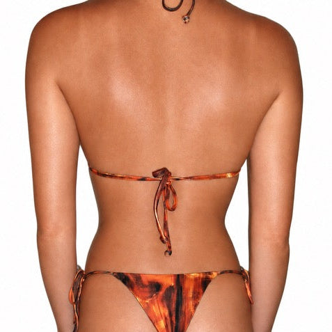 Rear view of a model wearing a string bikini with a fiery orange, brown, and black abstract pattern against a plain white background.